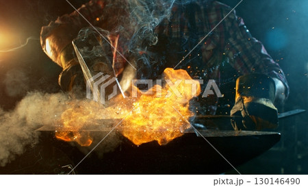 The blacksmith manually forging the molten metal on the anvil in smithy with spark fireworks 130146490