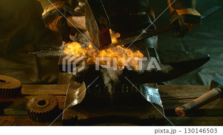 The blacksmith manually forging the molten metal on the anvil in smithy with spark fireworks 130146503
