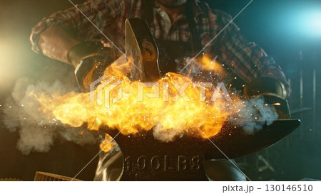 The blacksmith manually forging the molten metal on the anvil in smithy with spark fireworks 130146510
