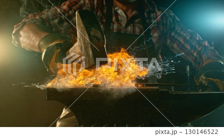 The blacksmith manually forging the molten metal on the anvil in smithy with spark fireworks 130146522