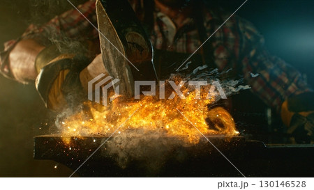 The blacksmith manually forging the molten metal on the anvil in smithy with spark fireworks The blacksmith manually forging the molten metal on the anvil in smithy with spark fireworks 130146528