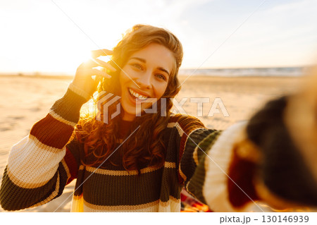 Young woman taking a cheerful selfie on a sandy beach during sunset. Lifestyle, travel, active life 130146939