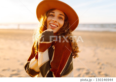 Young woman enjoying sunset at beach while wearing cozy striped sweater. Relax and lifestyle concept Young woman enjoying sunset at beach while wearing cozy striped sweater. Relax and lifestyle concept 130146944