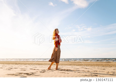 Stylish woman walks at sunset along beach of sea on at sunset. Travel, relax and lifestyle concept. Stylish woman walks at sunset along beach of sea on at sunset. Travel, relax and lifestyle concept. 130147111