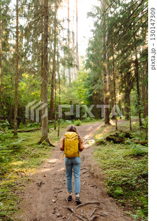 Tourist woman hiking alone in thick autumn forest. Stylish female looks for pathway among trees. 130147309