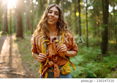 Tourist woman hiking alone in thick autumn forest. Stylish female looks for pathway among trees. 130147310