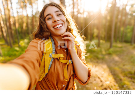Beautiful woman taking picture of herself while walking in sunny forest. Selfie in nature. Adventure 130147333