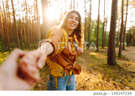 Traveling together. Happy woman holds the boyfriend's hand and walking on the forest. Vacation 130147334