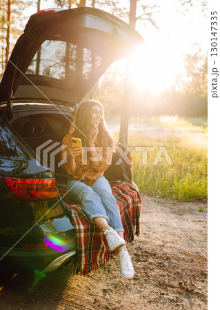 Young woman enjoys a sunny day outdoors while sitting in her car. Travel, weekend, nature, relax 130147335