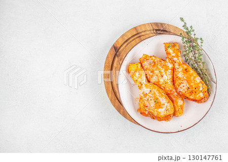 Raw marinated chicken drumsticks with spices and herbs on white plate. top view. copy space Raw marinated chicken drumsticks with spices and herbs on white plate. top view. copy space 130147761