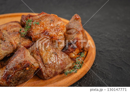 Close-up of grilled pork shashlik pieces on wooden plate with herbs 130147771