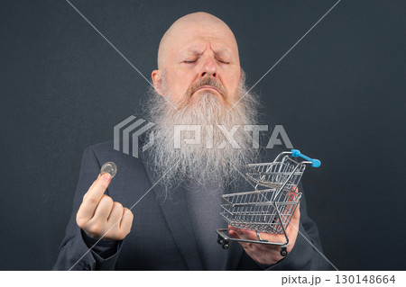 Elderly Man Examining a Coin Next to a Small Shopping Cart. Symbolizing Budgeting and Spending 130148664