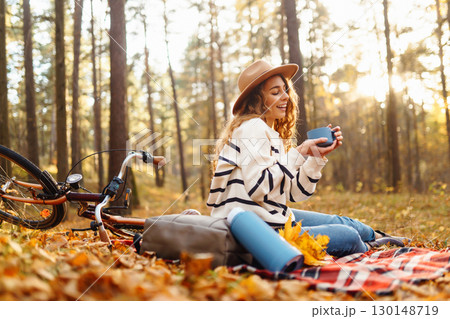 Relax in forest Woman sits on blanket, drinks from thermos, enjoys autumn atmosphere in sunny forest 130148719