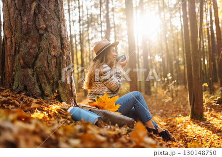 Cute young woman drinks hot drink from thermos and enjoys nature. Autumn landscape. relax concept. 130148750