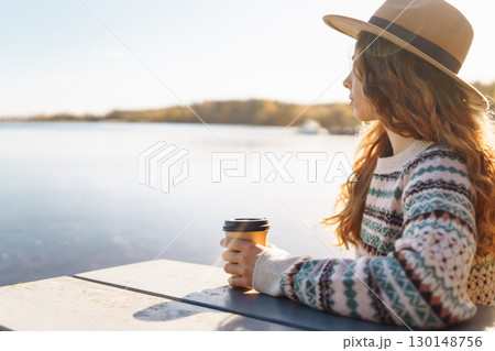 Fall concept woman drinking coffee on bench against backdrop of lake. Enjoying, solitude with nature Fall concept woman drinking coffee on bench against backdrop of lake. Enjoying, solitude with nature 130148756
