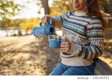 Lady drinks from thermo mug of coffee in nature. Warm up in sunny autumn forest. Travel, adventure. Lady drinks from thermo mug of coffee in nature. Warm up in sunny autumn forest. Travel, adventure. 130148761