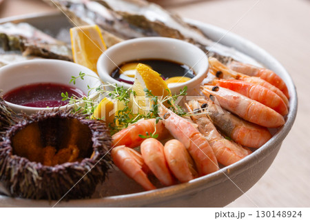 Seafood (oysters, shrimps, sea-urchins, mussels) are decoratively put on ice in a big plate Seafood (oysters, shrimps, sea-urchins, mussels) are decoratively put on ice in a big plate 130148924