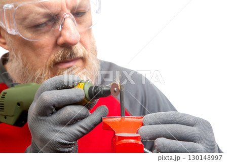 A skilled craftsman in safety goggles focuses intently on a rotary tool as he grinds a metal object 130148997