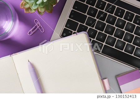 Notebook with pen near laptop keyboard, plant, and glass of water on purple desk. Place for your text Notebook with pen near laptop keyboard, plant, and glass of water on purple desk. Place for your text 130152413