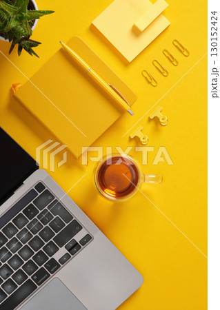 A tidy workspace with a laptop, a cup of tea, and office items in yellow colors. 130152424