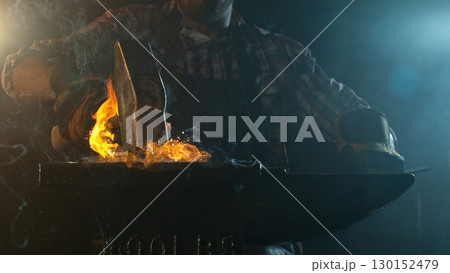 Close-up of blacksmith forging glowing hot iron on anvil with flying sparks 130152479