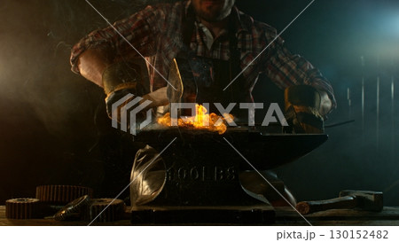 Close-up of blacksmith forging glowing hot iron on anvil with flying sparks Close-up of blacksmith forging glowing hot iron on anvil with flying sparks 130152482