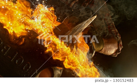 Close-up of blacksmith forging glowing hot iron on anvil with flying sparks Close-up of blacksmith forging glowing hot iron on anvil with flying sparks 130152483