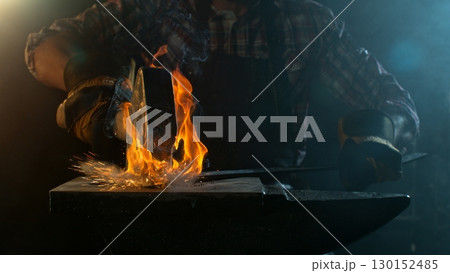 Close-up of blacksmith forging glowing hot iron on anvil with flying sparks Close-up of blacksmith forging glowing hot iron on anvil with flying sparks 130152485