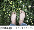 Girl's feet on Green Summer Grass with Field Flowers. Close-up Shot. Summer Time. Bare feet with white pedicures of a young woman. Enjoying the summer time. 130153270