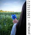 Side view portrait of a happy woman smelling lavender flowers bouquet in a field. young brunette woman with long hair holds a bouquet of blue wildflowers. Side view, woman in a field holding flowers 130153272