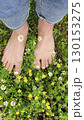 Girl's feet on Green Summer Grass with Field Flowers. Close-up Shot. Summer Time. Bare feet with white pedicures of a young woman. Enjoying the summer time. 130153275