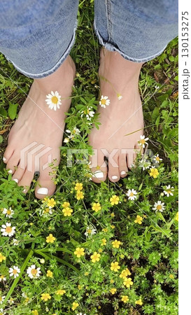Girl's feet on Green Summer Grass with Field Flowers. Close-up Shot. Summer Time. Bare feet with white pedicures of a young woman. Enjoying the summer time. Girl's feet on Green Summer Grass with Field Flowers. Close-up Shot. Summer Time. Bare feet with white pedicures of a young woman. Enjoying the summer time. 130153275