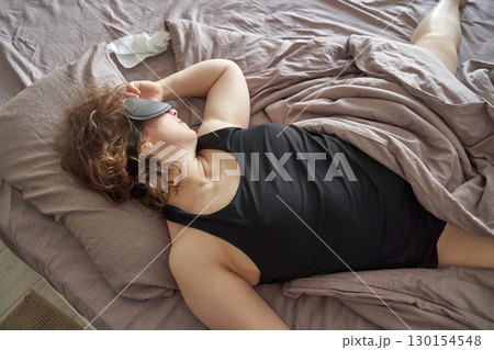 Caucasian female adult sleeping in bed wearing sleep mask on crumpled sheets 130154548