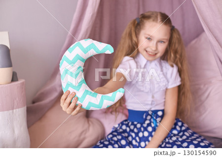 Young caucasian girl holding decorative crescent moon pillow in cozy room 130154590