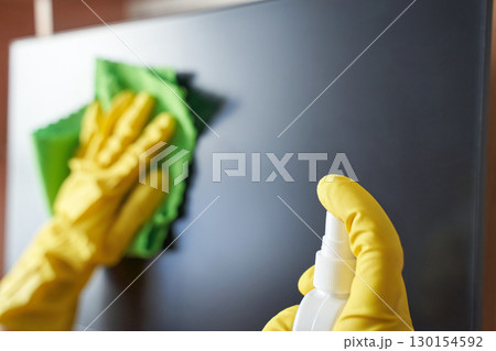 Close up of hands in yellow gloves cleaning a monitor with green cloth and spray Close up of hands in yellow gloves cleaning a monitor with green cloth and spray 130154592