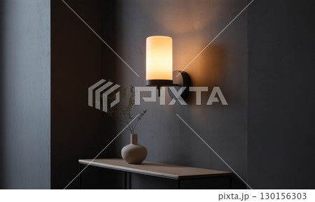 Minimalist modern wall sconce with glowing cylindrical glass shade on dark grey wall 130156303
