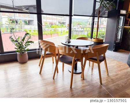 Round dining table with chairs near large window overlooking outdoor view. Hospitality, leisure, and social atmosphere for guests enjoying restaurant setting. 130157501