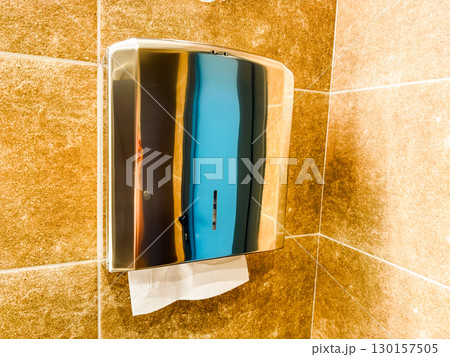 Metal dispenser with paper towel mounted on wall in restroom interior. Sanitation, hygiene, and guest service facility for cleanliness and convenience in hospitality. 130157505