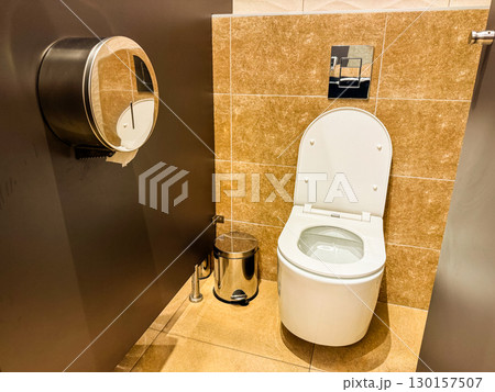 Public restroom interior with toilet and metal bin near tiled wall. Sanitation, hygiene, and facility design for cleanliness, comfort, and guest convenience. Public restroom interior with toilet and metal bin near tiled wall. Sanitation, hygiene, and facility design for cleanliness, comfort, and guest convenience. 130157507