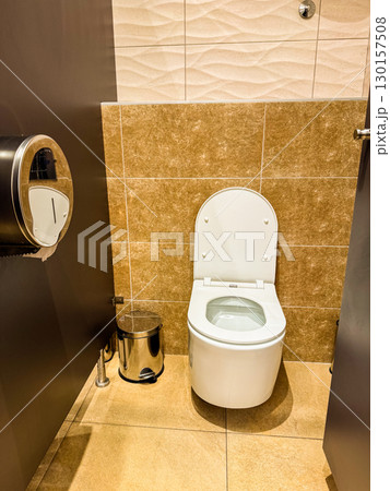 Public restroom interior with toilet and metal bin near tiled wall. Sanitation, hygiene, and facility design for cleanliness, comfort, and guest convenience. 130157508