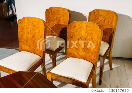 Set of four wooden vintage chairs with white upholstered seats arranged beside a polished table. Pre-owned elegance, upscale secondhand decor, vintage luxury, sustainable refinement Set of four wooden vintage chairs with white upholstered seats arranged beside a polished table. Pre-owned elegance, upscale secondhand decor, vintage luxury, sustainable refinement 130157620