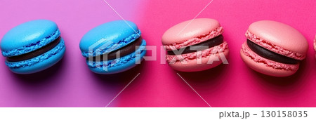 Colorful macarons displayed on vibrant pink and purple background at a dessert showcase 130158035