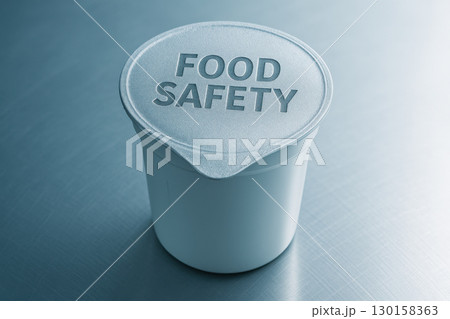 Yogurt cup with food safety engraved on foil lid standing on stainless inspection table with cold white laboratory lighting 130158363