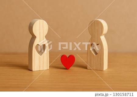 Wooden figurines with heart shaped cutouts facing each other with small red heart symbol between them, symbolizing love and relationship connection. Warm wooden texture and simple design 130158711
