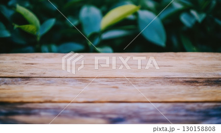 Wooden table surface surrounded by lush green foliage during bright daylight 130158808