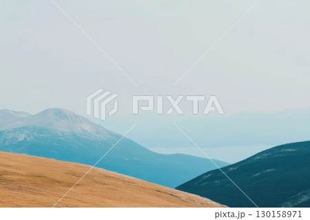 Mountain landscape with rolling hills and distant water view under a hazy sky during daylight 130158971
