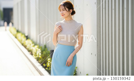 夏の日差しを浴びながら壁際で微笑む40代のきれいめ女性 130159342