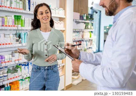 Male pharmacist talking to a woman and making notes Male pharmacist talking to a woman and making notes 130159483
