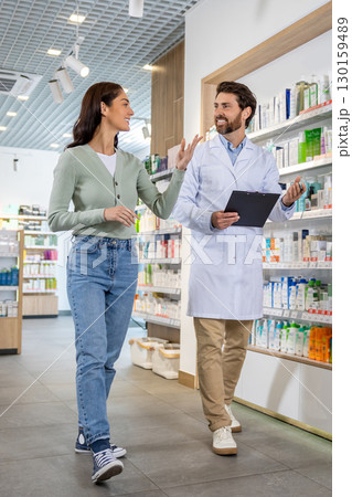 Pharmacy assistant with a notepad in hands talking to a female client Pharmacy assistant with a notepad in hands talking to a female client 130159489