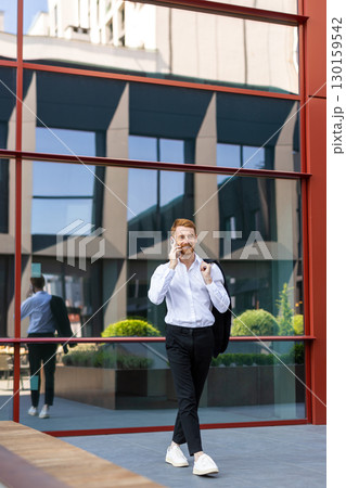 Stylish redhead in formal attire communicating on smartphone while walking Stylish redhead in formal attire communicating on smartphone while walking 130159542